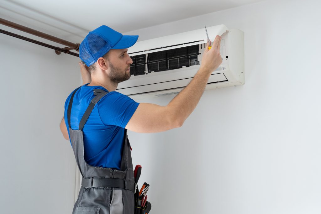 male technician overalls blue cap repairs air conditioner wall